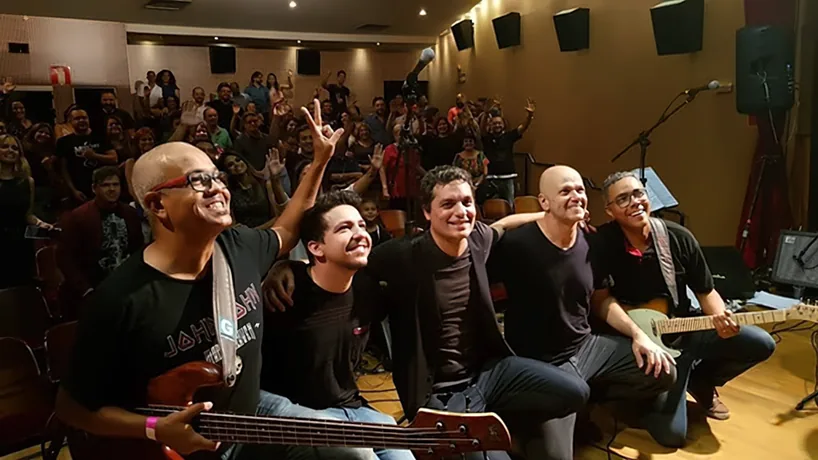 Aldrin Gandra e banda sentados no palco do Cine Theatro Brasil, com a plateia ao fundo